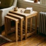 A set of three graduated bamboo nesting tables stacked together next to an armchair in a small, cozy apartment living room.