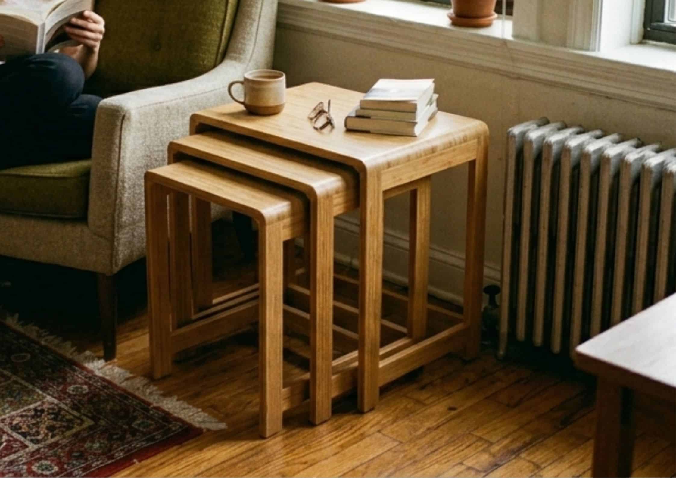 A set of three graduated bamboo nesting tables stacked together next to an armchair in a small, cozy apartment living room.